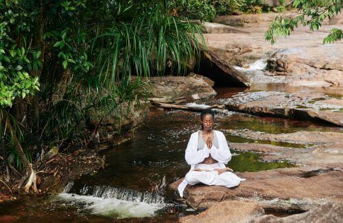 A person meditating near by the small river, serene nature.