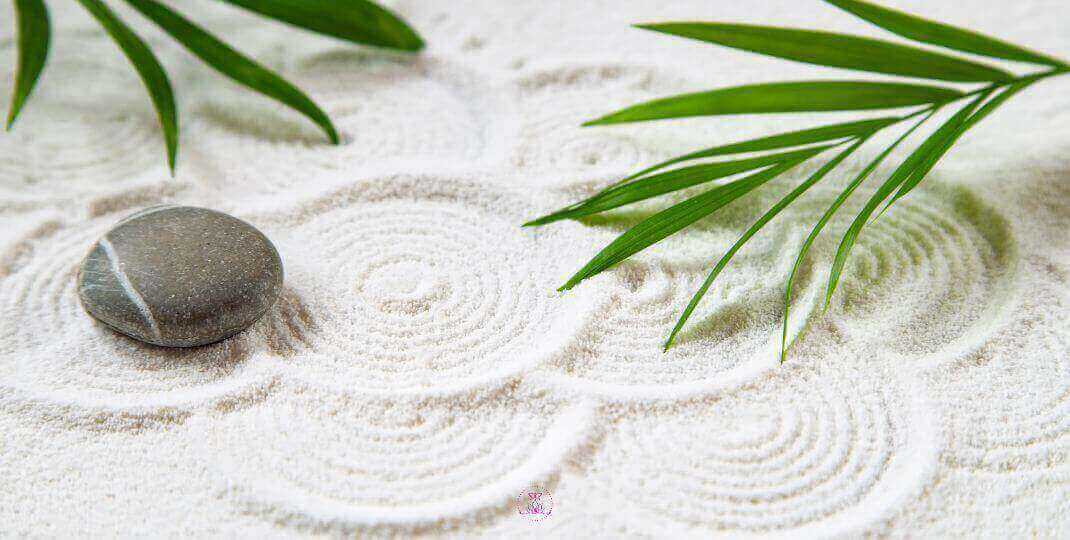 Zen garden with raked patterns in sand with green leaves