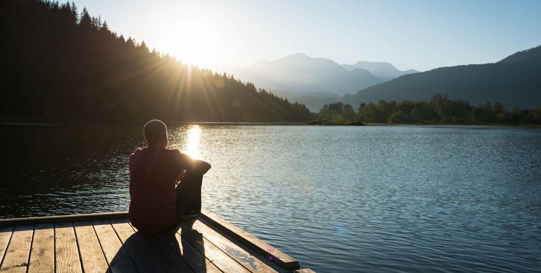 A person meditating in nature, near by the lake.