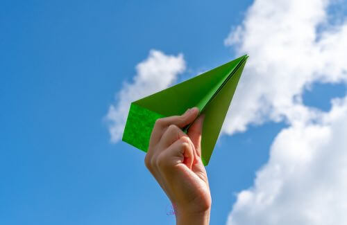 A person releasing a paper airplane into the sky.