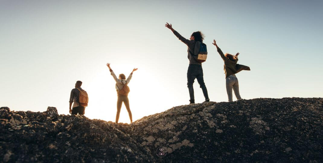 Persons are standing on top of a mountain, arms lifted in triumph