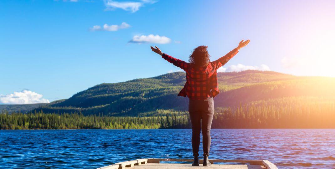 A person standing with arms wide open, basking in the beauty of nature, symbolizing the abundance of the universe.