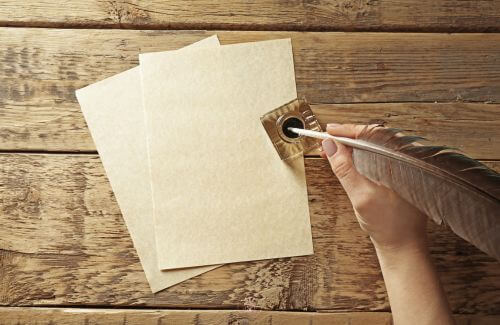 A person holding a quill pen poised above the blank page.