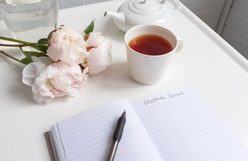 Give What You Want to Receive - An open journal with a pen beside it, placed on a wooden table, with a warm cup of tea or coffee nearby.