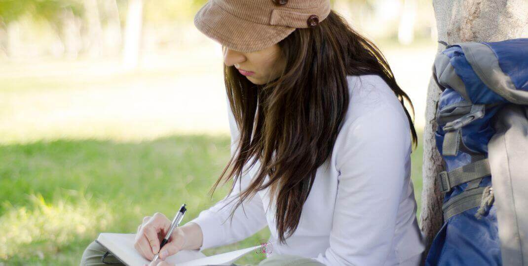 Learning from Experience - A woman sitting peacefully near a lake at sunrise, journaling with a calm expression.