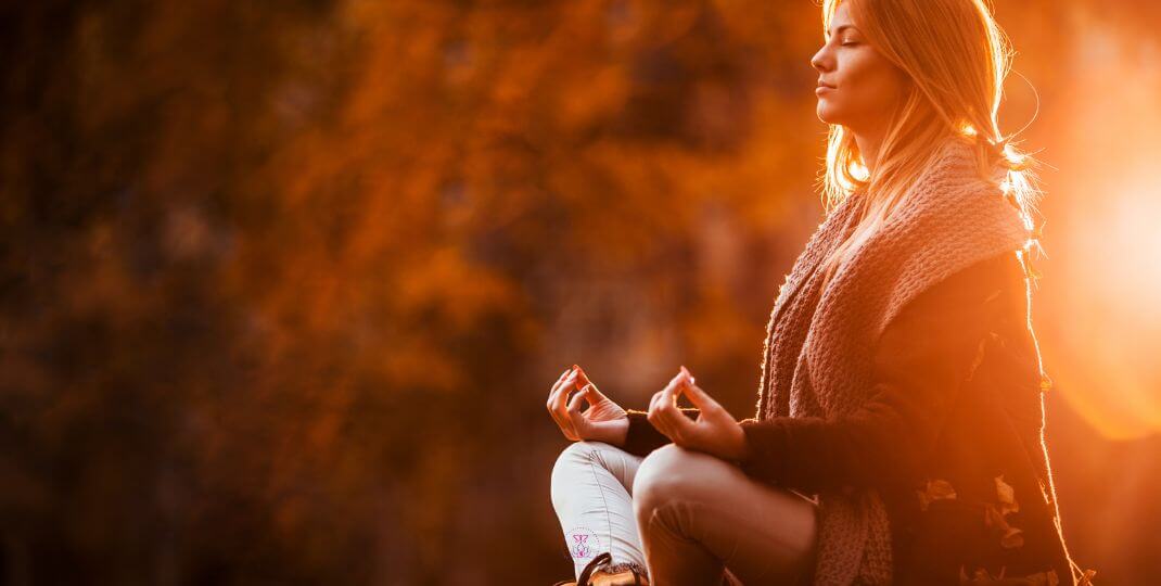 Finding balance in life - Image of a woman meditating outdoors, sitting under a tree, with soft sunlight.