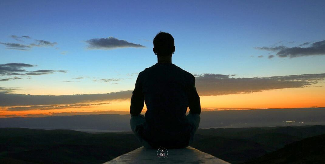 What You Focus on Becomes Reality - A person meditating at sunrise, with rays of light breaking through the horizon.