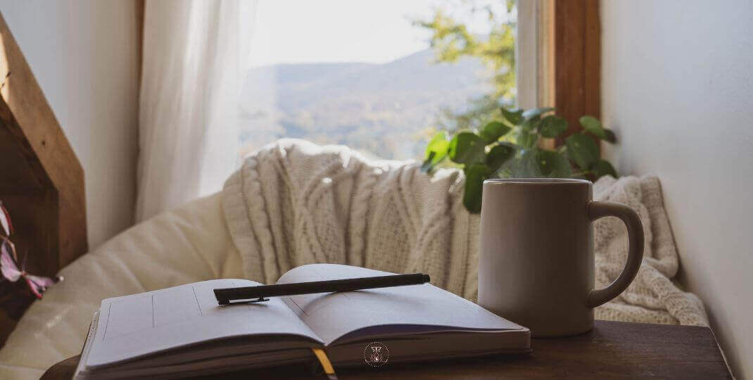 Power of Personal Choice - An open journal with a pen beside a cup of tea, is placed on a wooden table near a window.