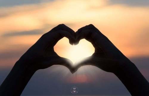 The Energy of Words - Two hands forming a heart shape, with a glowing light at the center, representing the connection built through honest and kind communication.