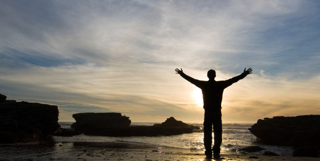 Let Go and Heal Now - A person standing by the ocean at sunrise, arms open wide