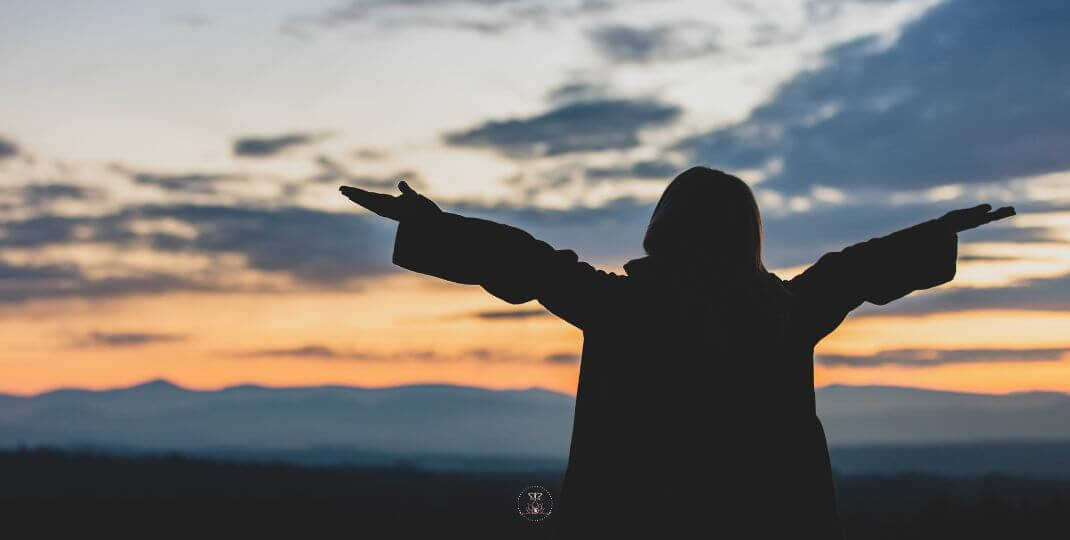 Let Go and Heal Now - A person standing on a hill at sunrise, arms open wide